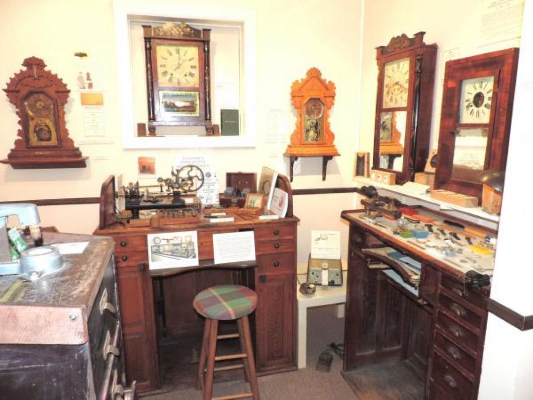 Old work benches and watch/clock repair tools display, early Nova Scotia and New Brunswick clocks in background.